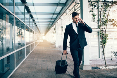 Handsome young man on business trip walking with his luggage and talking on cellphone at airport. Travelling businessman making phone call.